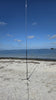 Radioddity HF-010 vertical antenna on a tripod base in the sand at Sunshine Skyway Fishing Pier State Park, with Tampa Bay and a distant island under a blue, partly cloudy sky behind it.