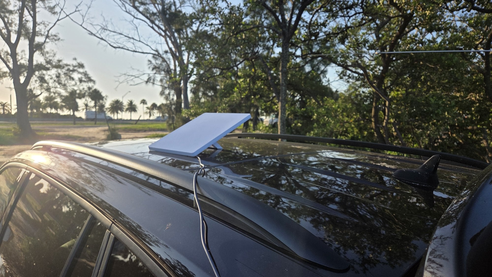 Starlink Mini mounted flat on the roof of the operating vehicle at Sunshine Skyway Fishing Pier State Park, morning sun through the trees behind it.
