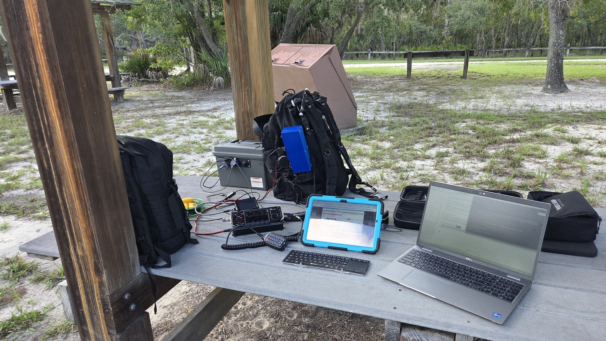 Portable station set up on a picnic table under an open-sided park shelter at Chassahowitzka WMA: tablet, laptop, radio and backpack on the table, pine flatwoods behind.